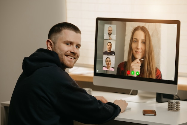 Foto lavoro a distanza. una vista posteriore di un uomo durante una videochiamata con i suoi colleghi sul computer desktop. un compagno distratto e sorride da un briefing online a casa.