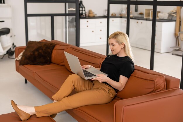 Remote work at home, freelance during covid-19 quarantine. Smiling lady sitting and working on laptop in cozy living room interior, free space.