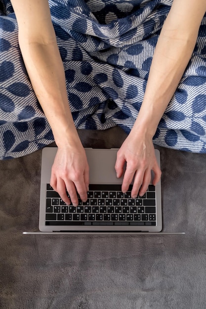 Remote work A woman works on a laptop wrapped in a plaid sitting on a soft couch at home