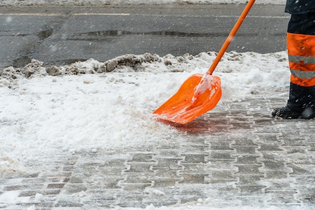 Removing snow from the sidewalk after snowstorm A road worker with a shovel in his hands and in special clothes cleans the sidewalk and the road from snow Snowstorm and hurricane in the city