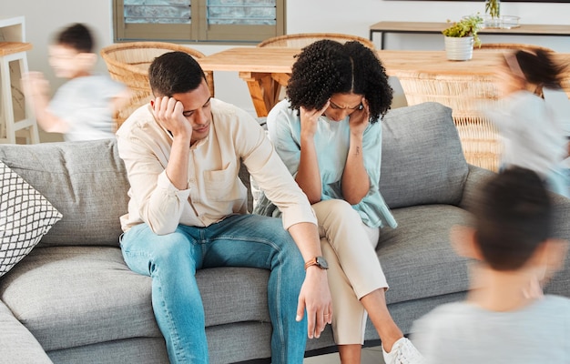 Rennende kinderen en vermoeide ouders op de bank met stress of chaos in de woonkamer gezinswoning en kinderen in huis met energie Uitgeputte burn-out en gefrustreerd zwart stel op de bank met jong kind