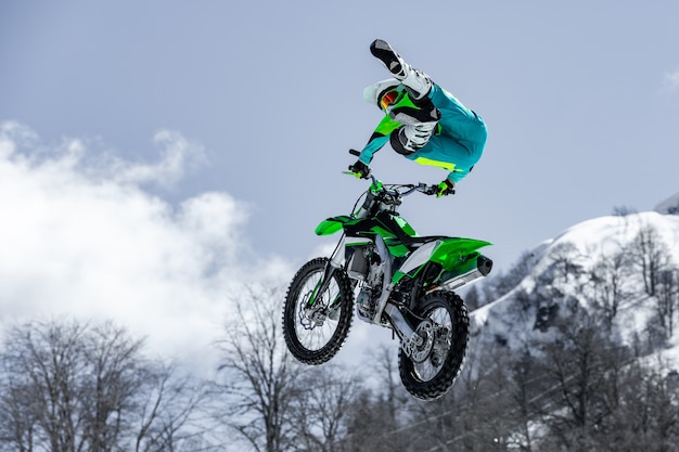 Renner op een motorfiets tijdens de vlucht, springt en stijgt op een springplank tegen de besneeuwde bergen