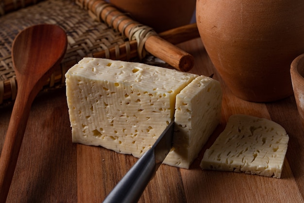 Rennet cheese being sliced on wooden table