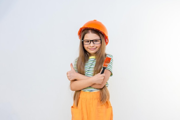 Renovatie in het appartement. Renovatie in de kinderkamer. Een klein meisje in een bouwhelm met een borstel in haar handen.