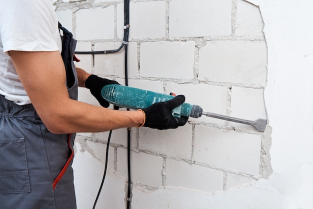 Renovation concept. Man with demolition hammer remove stucco from wall