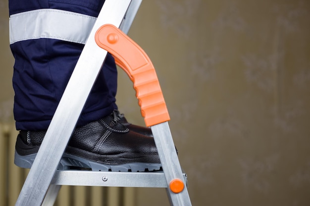 Foto concetto di ristrutturazione utilizzando una scala pieghevole in metallo un operaio in uniforme su una scala ripara