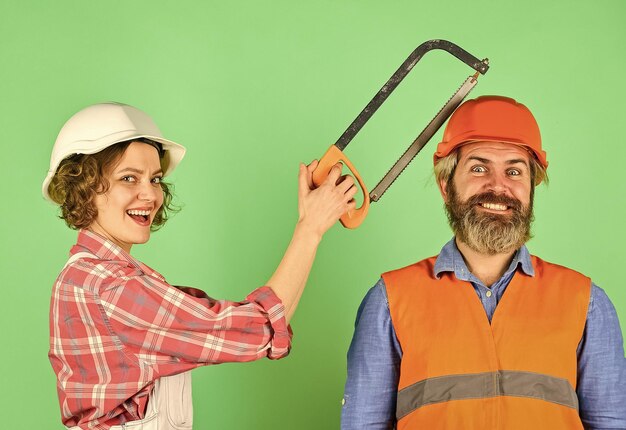 Renovation is struggle Annoying edits Couple renovating home Man and woman wear safety helmet Home Renovation She is sawing him Hand Saw tool Sawing husband head Annoyed by her actions