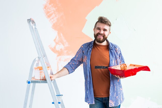 Photo renovation, redecoration and repair concept - cheerful guy painting wall in new home.