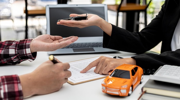 The renter is signing a car rental agreement with the car rental company. After discussing the details and charges with the employee, the employee hand over the car keys to the renter.