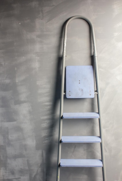 Repair in an apartment by using a stepladder which stands leaning on painted gray wall