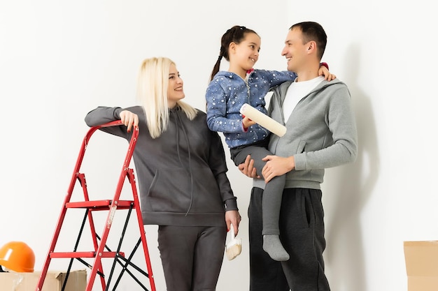 Repair in the apartment. Happy family mother, father and child daughter paints the wall with paint.