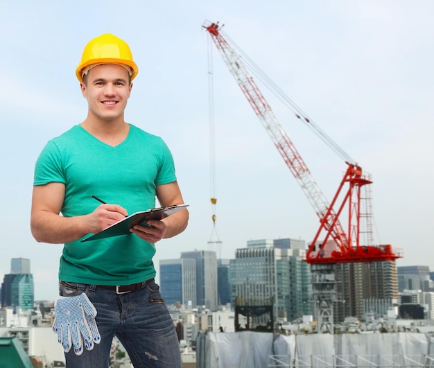 repair, building, construction and maintenance concept - smiling man in helmet with clipboard making notes