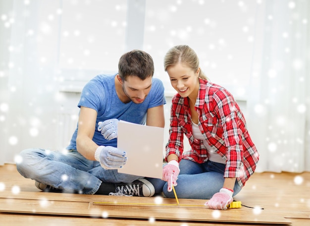 修理、建物、家族、人々、家のコンセプト-床に寄木細工の板を測定する笑顔のカップル