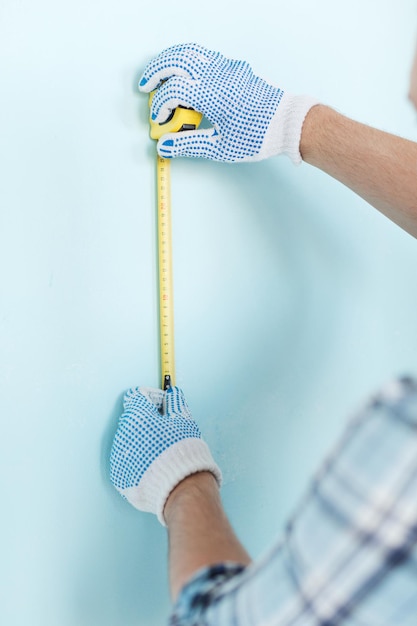 repair, building and home concept - close up of male in gloves measuring wall with tape