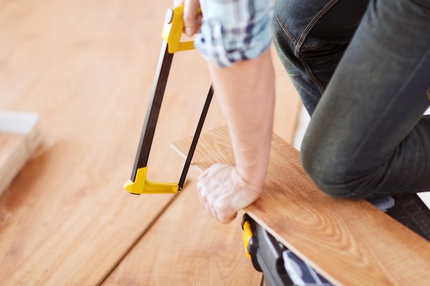 Photo repair, building and home concept - close up of male hands cutting parquet floor board with saw