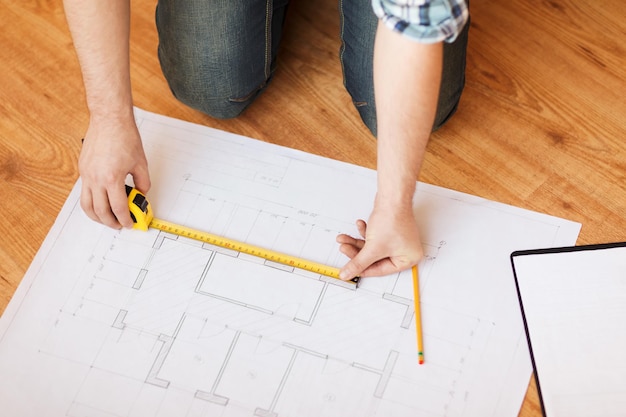 repair, building and home concept - close up of male hands measuring blueprint