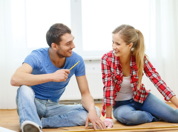 repair, building and home concept - smiling couple measuring wood flooring