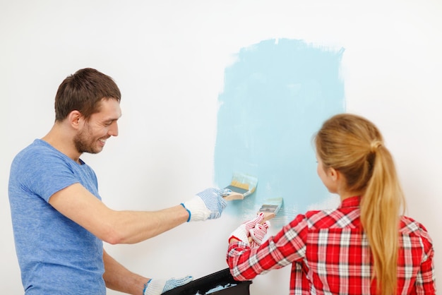 repair, building and home concept - smiling couple painting wall at home