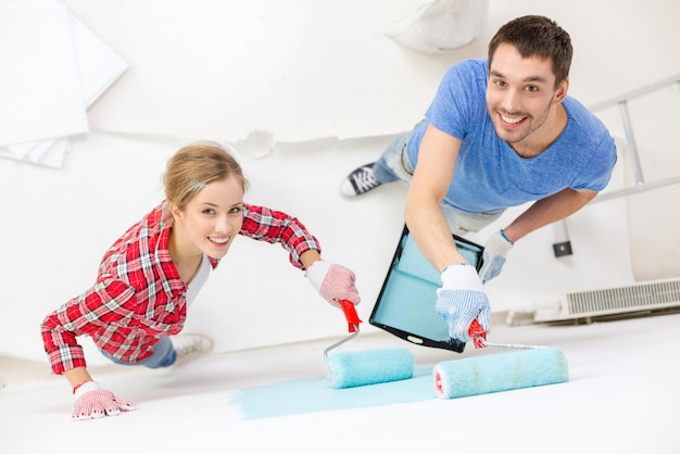 repair, building and home concept - smiling couple painting wall at home