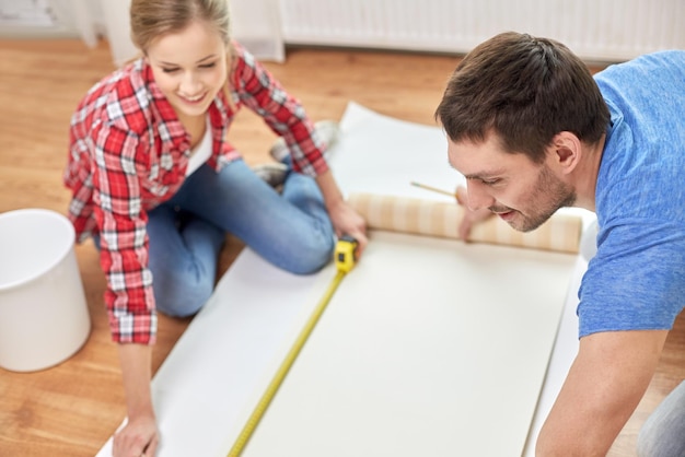 Photo repair, building and people concept - close up of couple with ruler measuring wallpaper at home