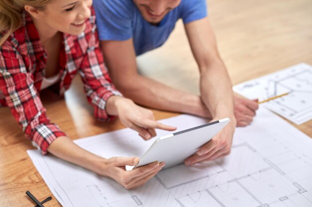 repair, building, renovation, architecture and technology concept - close up of couple with tablet pc and blueprint at home