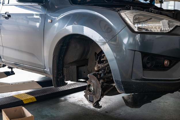 Repair and change parts a pickup truck with damaged axle and wheel lifted by scissor lift in garage