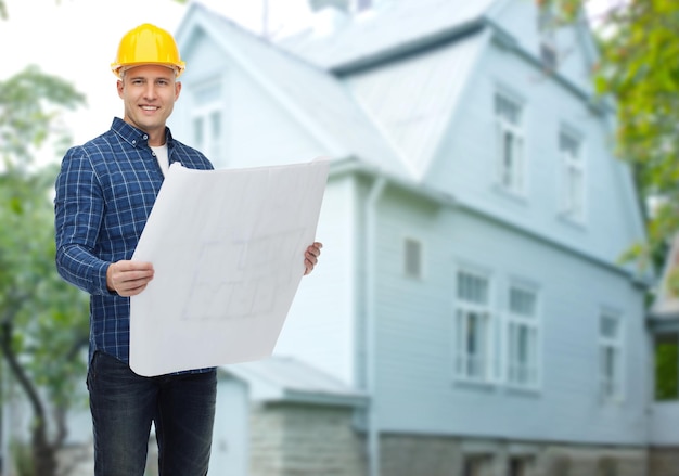 концепция ремонта, строительства, строительства, людей и технического обслуживания - улыбающийся мужчина-строитель или рабочий в шлеме с чертежом на фоне живого дома