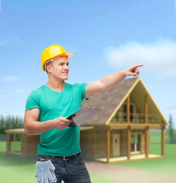 repair, construction and maintenance concept - smiling man in helmet with clipboard pointing finger