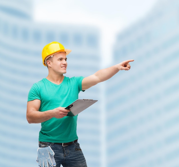 repair, construction and maintenance concept - smiling man in helmet with clipboard pointing finger