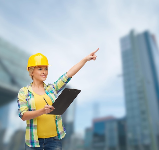 Concetto di riparazione, costruzione e manutenzione - donna sorridente in casco con appunti che punta il dito