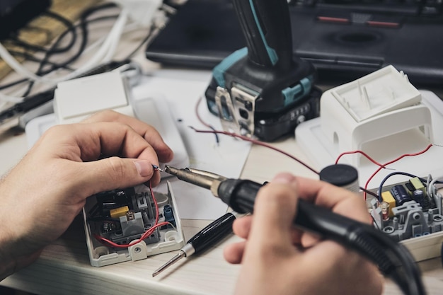 電子機器、スズはんだ部品の修理。ドライバーを持っている男の手。コンピュータ回路基板