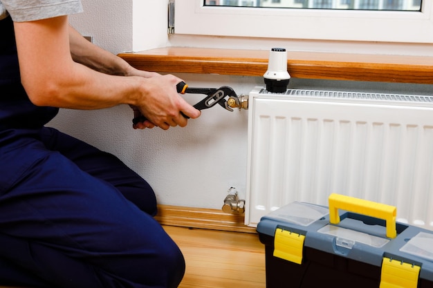 Repair heating radiator closeup man repairing radiator with\
wrench removing air from the radiator