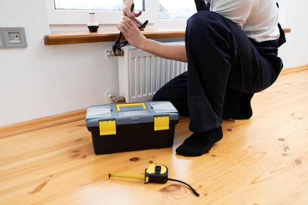 Repair heating radiator closeup man repairing radiator with\
wrench removing air from the radiator