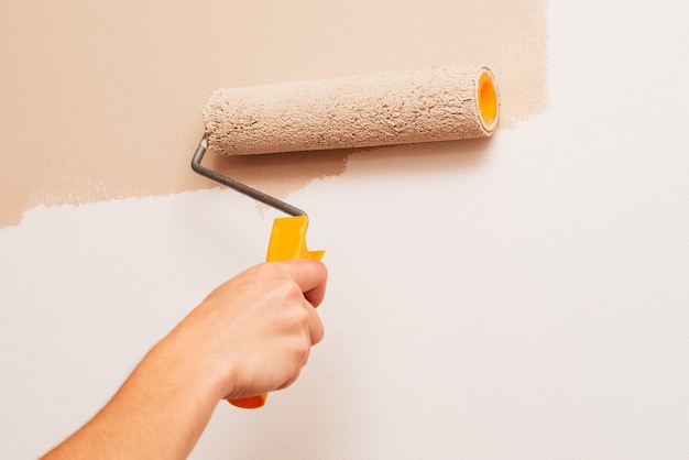 Repair in the house. A man paints the walls with a roller in beige color