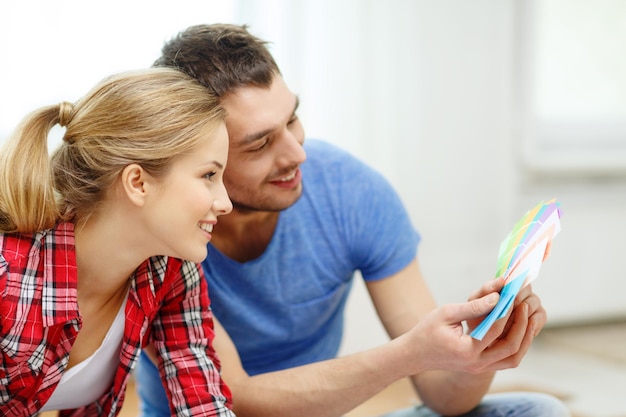 repair, interior design, building, renovation and home concept - smiling couple looking at color samples at home