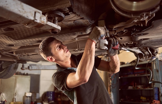 Premium Photo  Repair man fixing car in repair station under lifted car  during repair in garage