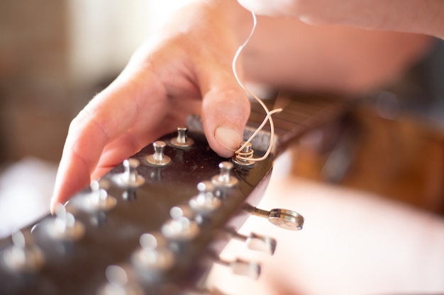 Repair of an old guitar. The man pulls the strings on the fretboard. Selective focus.