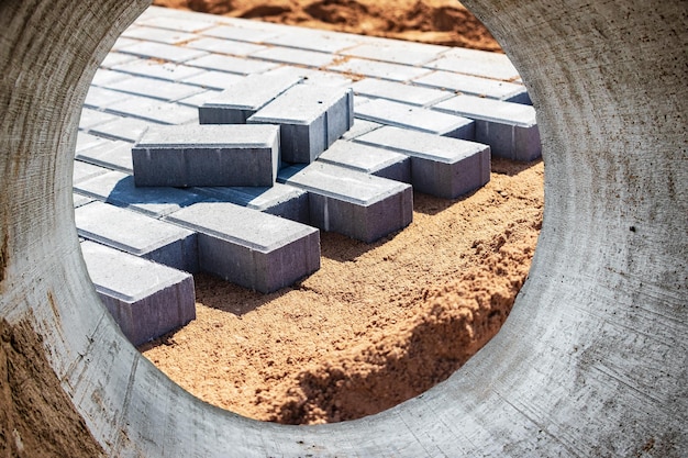 Repair of the road surface and laying paving slabs on the\
prepared surface laying paving slabs closeup arrange the sidewalk\
in the city paving slabs and curbs view from a large pipe