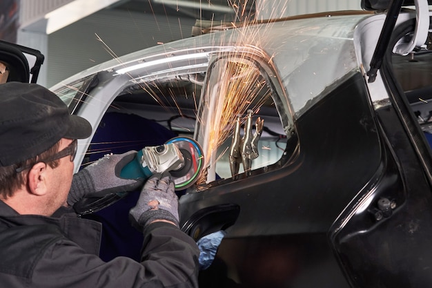 Automobile danneggiata della riparazione del lavoratore di servizio di riparazione lavorare con smerigliatrice angolare per fissare il corpo in metallo.