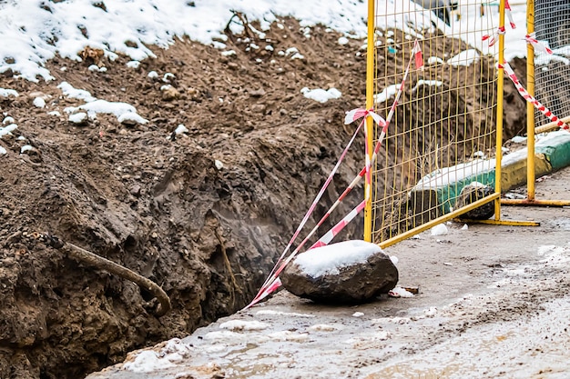 Repair of underground utilities in winter Ditch in ground fenced off with grate Abandoned construction site