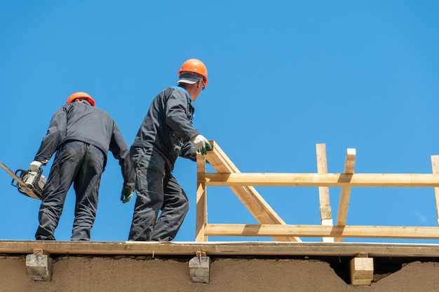 Repair of a wooden roof outdoors against a blue sky background Two carpenters in special clothes work at a height Roofing contractors are preparing the roof for the installation of insulation