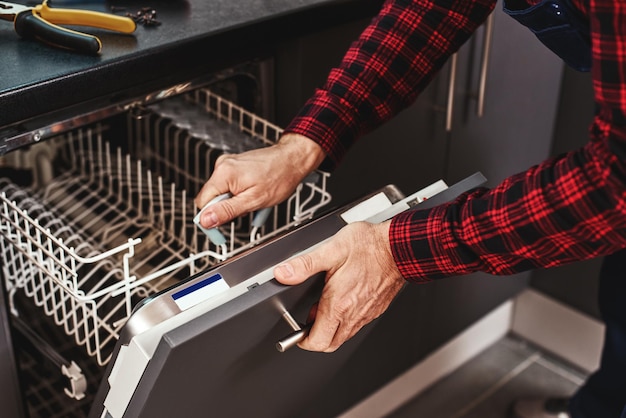 Repairing dishwasher closeup of man technician sitting near dishwasher