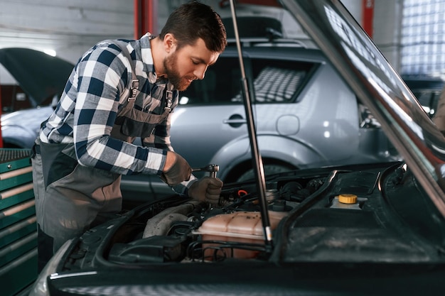 Photo repairing the electronics of the car under the hood man in uniform is working in the auto salon