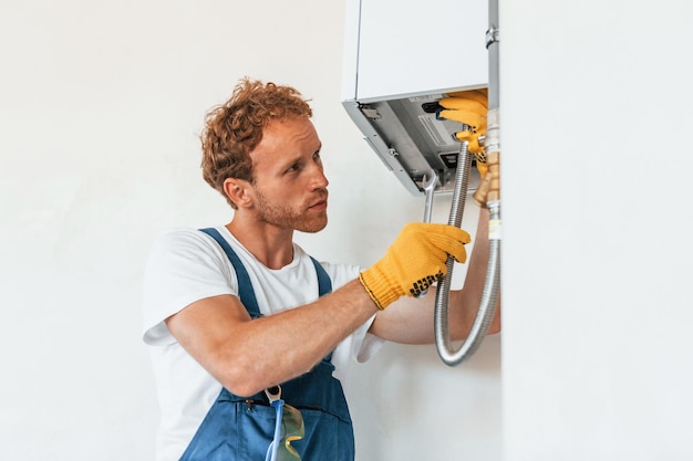 Repairing water heater Young man working in uniform at construction at daytime