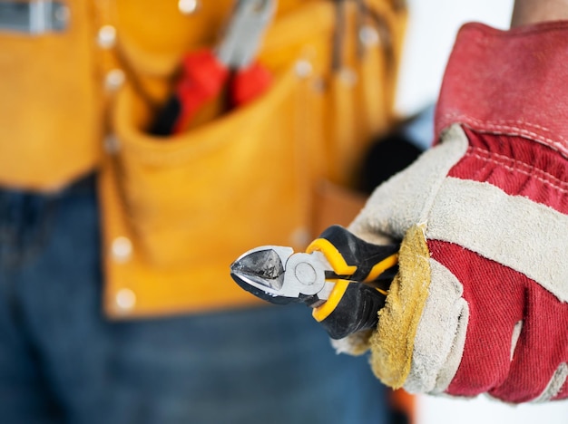 Repairman in assembly belt and protective gloves holding side\
cutters in hand