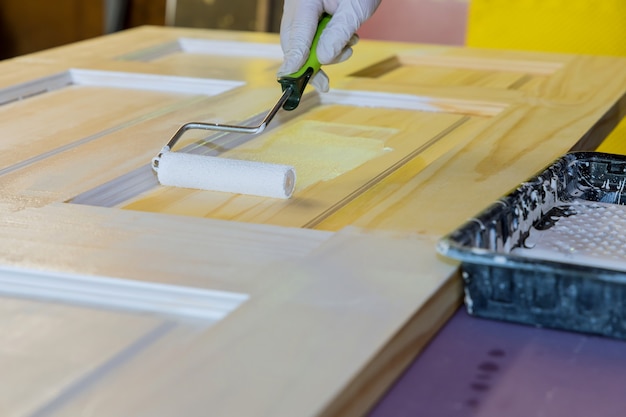 Repairman carpenter working painting a wooden door using hand roller