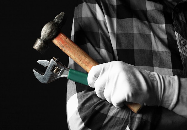 La mano del riparatore nei guanti si chiude con gli strumenti della chiave e del martello su sfondo nero.