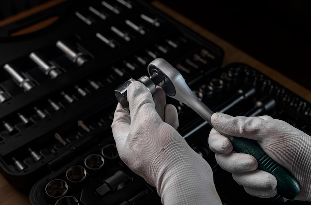 Repairman hand in white glove with socket ratchet handle and metal steel hex socket, closeup. Car repair metal tools.