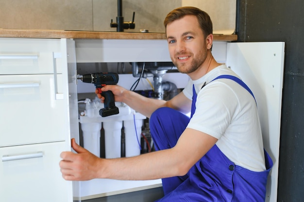 Photo repairman in overalls repairing cabinet hinge in kitchen