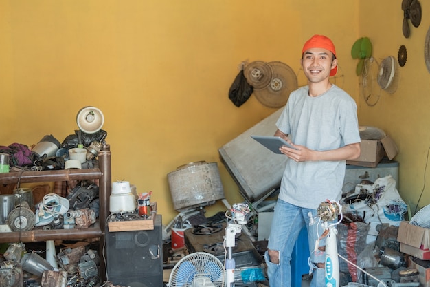 repairman smiles at the camera while using his tablet pc around electronic parts in the service shop room